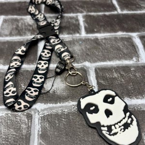 Puede incluir: Cordón negro con un patrón repetido de calaveras blancas. Un dije en forma de calavera en blanco y negro está unido con un cierre y un anillo de metal. El cordón tiene una hebilla de plástico negro.