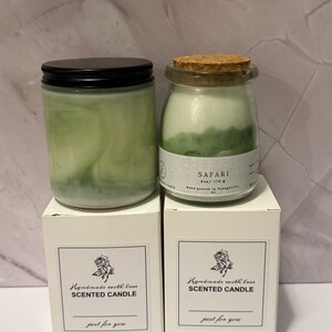 K&ouml;nnte beinhalten: Zwei gr&uuml;n get&ouml;nte Duftkerzen in Gl&auml;sern mit schwarzen Deckeln und Korken, auf wei&szlig;en Schachteln. Auf den Schachteln steht "Handmade with love SCENTED CANDLE just for you."