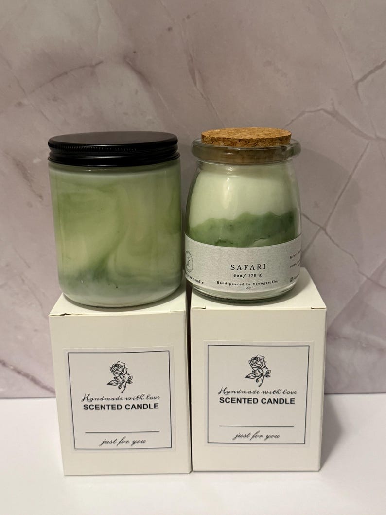 K&ouml;nnte beinhalten: Zwei gr&uuml;n get&ouml;nte Duftkerzen in Gl&auml;sern mit schwarzen Deckeln und Korken, auf wei&szlig;en Schachteln. Auf den Schachteln steht "Handmade with love SCENTED CANDLE just for you."