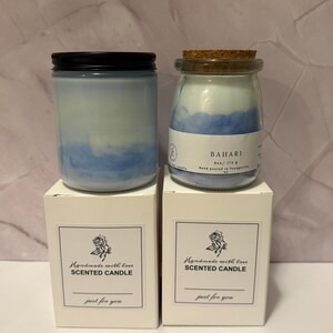 K&ouml;nnte beinhalten: Zwei Duftkerzen in Gl&auml;sern mit blauem und wei&szlig;em Wachs, eine mit schwarzem Deckel und die andere mit Korken. Die Gl&auml;ser stehen auf wei&szlig;en Schachteln mit dem Text "Handmade with love Scented Candle just for you."