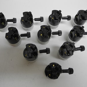 Op de afbeelding: Een verzameling zwarte en zilveren lampfittingen met een zwarte knop. De fittingen hebben een schroefbasis en zijn ontworpen om een gloeilamp vast te houden. De afbeelding toont een close-up van de fittingen.