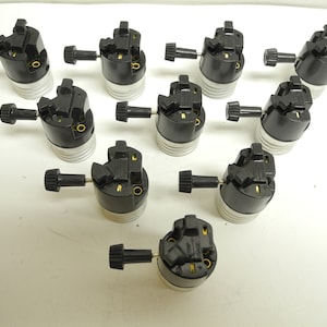 May include: A collection of black and silver light bulb sockets with a twist knob. The sockets have a black plastic housing and a silver base. The knobs are black and have a ridged design. The sockets are arranged on a white surface.