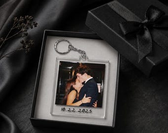 Op de afbeelding: Een vierkante sleutelhanger van helder acryl met een afgedrukte foto van twee mensen die elkaar omhelzen, met de datum 10.22.2025 in zwarte inkt onderaan. De sleutelhanger heeft een zilverkleurige metalen ring en zit in een zwarte geschenkdoos.