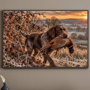 May include: A framed wall art print depicting a brown and white wirehaired dog standing in a frost-covered field at sunrise, carrying a pheasant in its mouth. The scene features golden light, rolling hills, and dense, icy vegetation.