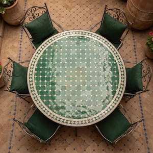 May include: A round dining table with a green and white geometric tiled top, surrounded by four dark metal chairs. Each chair features a dark green square cushion. The table surface displays a repeating pattern of small white squares.