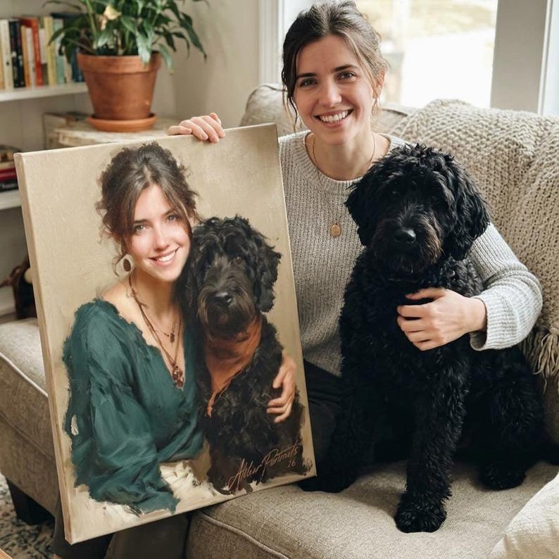 May include: A canvas portrait of a woman and a black dog. The woman in the portrait wears a green top and the dog has a red scarf. A real black dog sits next to the portrait. The portrait is signed.