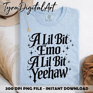 May include: Pale blue t-shirt featuring the phrase "A Lil Bit Emo A Lil Bit Yeehaw" in black lettering. The shirt has a round neck and is displayed with a hat and sandals.