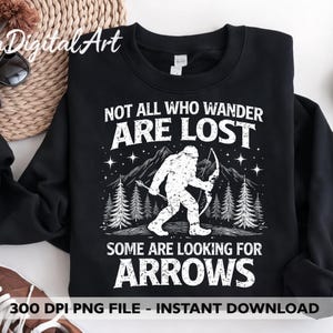 Op de afbeelding: Zwart sweatshirt met een witte afbeelding van een Bigfoot met pijl en boog, bergen en bomen. De tekst luidt: "NOT ALL WHO WANDER ARE LOST, SOME ARE LOOKING FOR ARROWS."