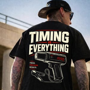 Puede incluir: Camiseta negra con la frase "TIMING IS EVERYTHING" en letras blancas. Debajo, un gráfico de una luz de sincronización con el texto "FOCUS. PRECISION. RESULTS."