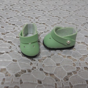 May include: A pair of light green leather doll shoes with a white pearl accent on one shoe.