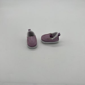 May include: A pair of lavender slip-on shoes with white soles and faux fur lining. The shoes have a stitched design and a small pull tab at the heel. These shoes are designed for a child.