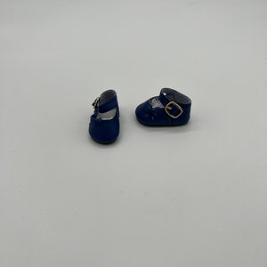 May include: A pair of dark blue leather doll shoes with gold buckles.