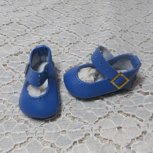 May include: A pair of blue leather baby shoes with gold buckles. The shoes have a strap across the top and are closed toe.