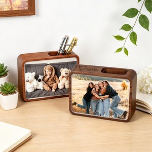 May include: Two wooden desk organizers. One displays a photo of four women, the other features a baby in a brown outfit with stuffed animals. Both have pen holders and are on a wooden desk.