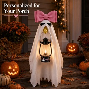 May include: A white ghost decoration featuring a large pink bow on top and a black lantern held in the center. The lantern base is personalized with the name Avery and a small ghost icon. The text Personalized for Your Porch appears above.
