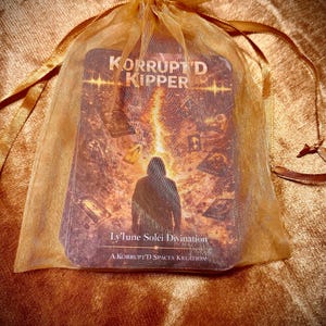 May include: A deck of cards titled KORRUPT'D KIPPER inside a sheer gold organza drawstring bag. The top card features a hooded figure standing before a fiery explosion with smaller cards floating around, labeled Ly'lune Soléi Divination.