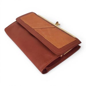 May include: A brown leather wallet with a bi-fold design. The wallet features a lighter brown patch on the flap and a gold-coloured clasp. The wallet is made of leather and has a classic, timeless design.