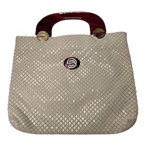 Puede incluir: Bolso de mano blanco roto con un exterior texturizado con patrón de diamantes. Cuenta con un asa curva de color rojo oscuro y herrajes dorados. Un emblema circular con la letra "S" está centrado en la parte delantera.