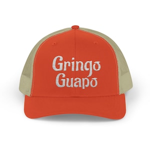 May include: A trucker hat with a bright orange front panel and a tan mesh back. The hat features the embroidered words "Gringo Guapo" in white, a playful and eye-catching design.