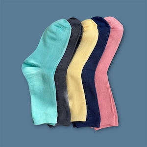 May include: A set of five ribbed crew socks arranged in a fan shape, featuring a variety of solid colors including light turquoise, dark charcoal gray, pale yellow, navy blue, and soft pink, all made with a consistent knit texture throughout.