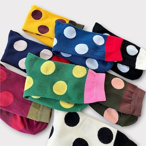 Op de afbeelding: Een verzameling kleurrijke sokken met grote stippen. De sokken zijn in verschillende kleuren, waaronder geel, blauw, groen en zwart, elk met contrasterende stippen. De sokken zijn gemaakt van een zacht materiaal en zijn opgevouwen.