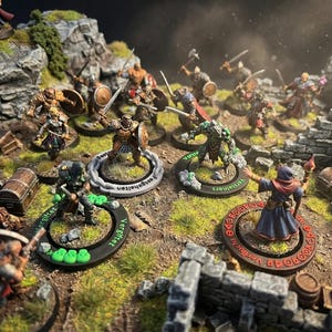 May include: Miniature fantasy figures of warriors and monsters are arranged on a diorama base with rocks, grass, and ruins. The figures are painted in various colors and poses, with swords, shields, and magic. Some figures have text on their bases.