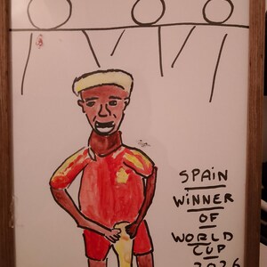 Peut inclure: Un dessin encadré représentant une personne en maillot rouge et jaune tenant un trophée. Au-dessus se trouvent trois personnages en bâton. Le texte indique : SPAIN WINNER OF WORLD CUP 2026. L'œuvre est réalisée au feutre sur fond blanc avec un cadre en bois.