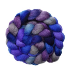 May include: A vibrant, hand-dyed roving yarn in shades of blue, purple, and gray. The yarn is arranged in a circular braid, showcasing the color variations. This fiber is suitable for various fiber art projects.