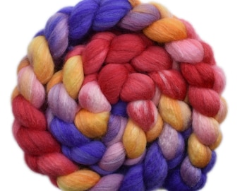Può includere: Primo piano di un gomitolo di filato colorato in tonalità di viola, rosso, arancione e giallo. Il filato è intrecciato e attorcigliato, creando un effetto visivo e testurale accattivante.