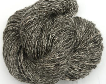 Puede incluir: Un ovillo de hilo de color gris oscuro con motas blancas. El hilo está hecho de lana y es adecuado para tejer o hacer ganchillo.