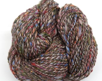 May include: A skein of yarn in a brown, blue, red, and green colorway with a speckled effect.