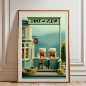 Könnte beinhalten: Ein gerahmter Kunstdruck mit einer Miniatur-Pub-Szene, bei der der Text PINT OF VIEW über zwei mit goldenem Bier und weißem Schaum gefüllten Glaskrügen steht, vor einem weichen blauen Hintergrund mit einer hellen Gebäudestruktur.