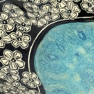 May include: A ceramic bowl featuring a central basin with a textured, mottled turquoise and light blue glaze. The wide, dark black rim is decorated with a repeating pattern of carved, cream-colored five-petaled flowers with dark centers.