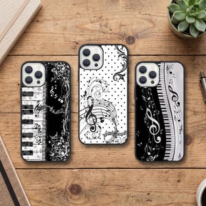 Puede incluir: Tres fundas rectangulares para smartphone con temas musicales en blanco y negro. La funda izquierda muestra teclas de piano y remolinos florales. La central muestra lunares, notas musicales y una clave de sol. La derecha muestra teclas de piano y notas.
