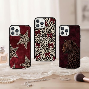 Op de afbeelding: Drie telefoonhoesjes met zwarte randen. Eén hoesje heeft een bordeauxrode achtergrond met luipaardprintsterren. Een andere heeft een luipaardprintpatroon met bordeauxrode strikken. De derde heeft een luipaard tegen een bordeauxrode achtergrond.