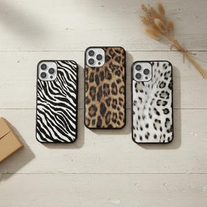 May include: Three mobile phone cases with animal print designs. One case has a black and white zebra pattern, another a brown and black leopard print, and the third a white and black snow leopard print. Each case has a black border.