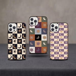 Può includere: Tre custodie per telefono con disegni celesti. Le custodie presentano motivi a scacchiera con lune, stelle e soli in vari colori, tra cui nero, crema, viola e arancione. Le custodie sono esposte su una superficie grigio scuro.