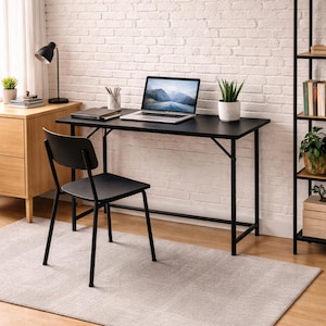 Könnte beinhalten: Ein schwarzer Schreibtisch mit einem schwarzen Stuhl, einem Laptop und einer kleinen Topfpflanze. Der Schreibtisch steht vor einer weißen Backsteinmauer. Ein Holzschrank und eine schwarze Lampe befinden sich links. Ein Teppich liegt auf dem Boden.