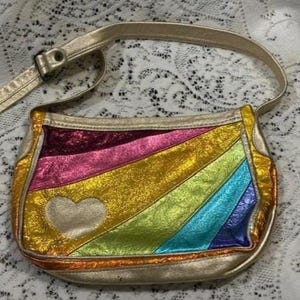 May include: A metallic shoulder bag featuring a diagonal rainbow pattern in shades of pink, yellow, green, blue, and purple. The bag has a gold-toned strap and a gold-toned heart-shaped appliqué on the front. The surface has a crinkled texture.