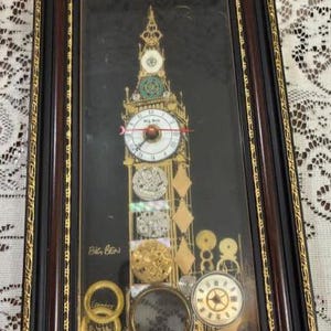 May include: A rectangular wall art piece featuring a gold-toned collage of Big Ben, constructed from various watch parts and gears on a black background. The artwork is encased in a dark brown wooden frame with gold trim and includes the text Big Ben.