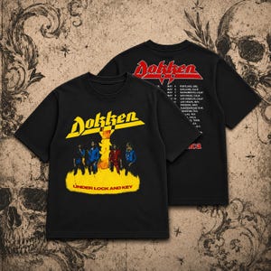 May include: A black short-sleeve t-shirt featuring the Dokken logo in yellow and red. The front displays a band graphic with the text Under Lock and Key. The back shows the Dokken logo in red and a list of tour dates and locations in white text.
