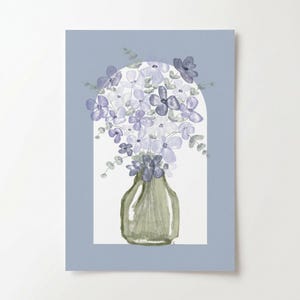 May include: Watercolour painting of a bouquet of purple and white flowers in a green vase. The vase is set against a white background within a light blue frame. The flowers have green stems and leaves. The artwork is a floral still life.
