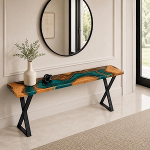 May include: A rectangular console table featuring a natural wood slab with a central river-like inlay of teal resin. The table is supported by two black metal X-shaped legs. A white ceramic vase with green foliage sits on the table surface.