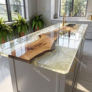 Puede incluir: Isla de cocina con encimera de resina epoxi transparente. La encimera presenta una losa de madera de borde vivo y un diseño de resina blanco crema y transparente. La isla tiene una base gris claro con herrajes dorados.
