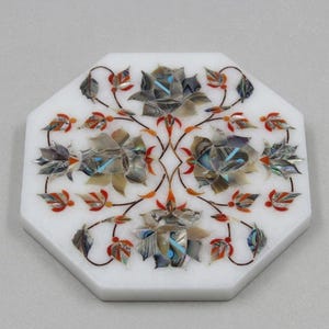May include: White marble octagonal decorative piece with inlaid floral design. The flowers are composed of iridescent shell pieces with accents of blue, orange, and red. The leaves and stems are dark brown.