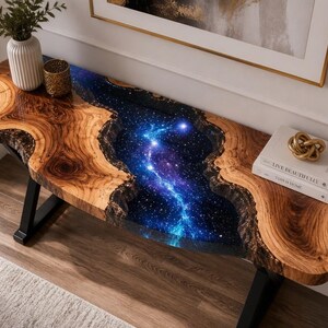 May include: A live edge wood console table featuring a central river design filled with blue and purple galaxy-themed resin. The table has black metal legs and is topped with a white vase, a gold candle holder, and two books labelled Live Beautifully.