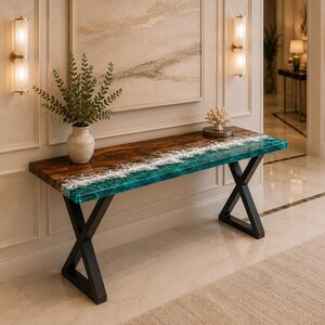 May include: A rectangular console table featuring a natural wood grain surface combined with a vibrant turquoise and white resin ocean wave design. The table is supported by two black metal X-shaped legs, creating a sturdy base for the tabletop.
