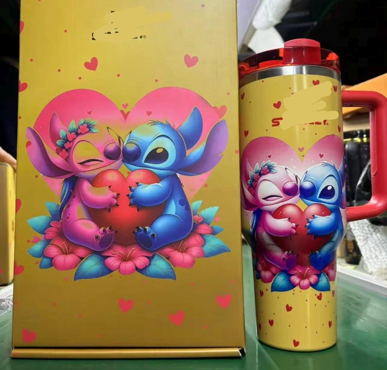 Pu&ograve; includere: Un set di bicchiere e scatola gialli con una coppia di cartoni animati che abbraccia un cuore. Il bicchiere ha un manico e un coperchio rossi. La scatola e il bicchiere hanno un motivo a cuore ripetuto.