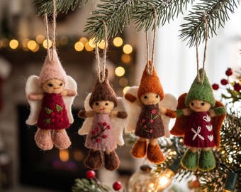 May include: Four felt angel ornaments hanging from a pine branch. Each angel features a pointed hat, white wings, and a dress with embroidered details. The figures are coloured in shades of pink, burgundy, brown, orange, and green with twine loops.