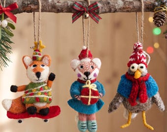 May include: Three needle-felted animal ornaments hanging from a branch. A fox on a red skateboard, a mouse in a blue dress holding a red gift, and a bird in a blue cape and red scarf. Each wears a small hat and hangs by a twine loop.